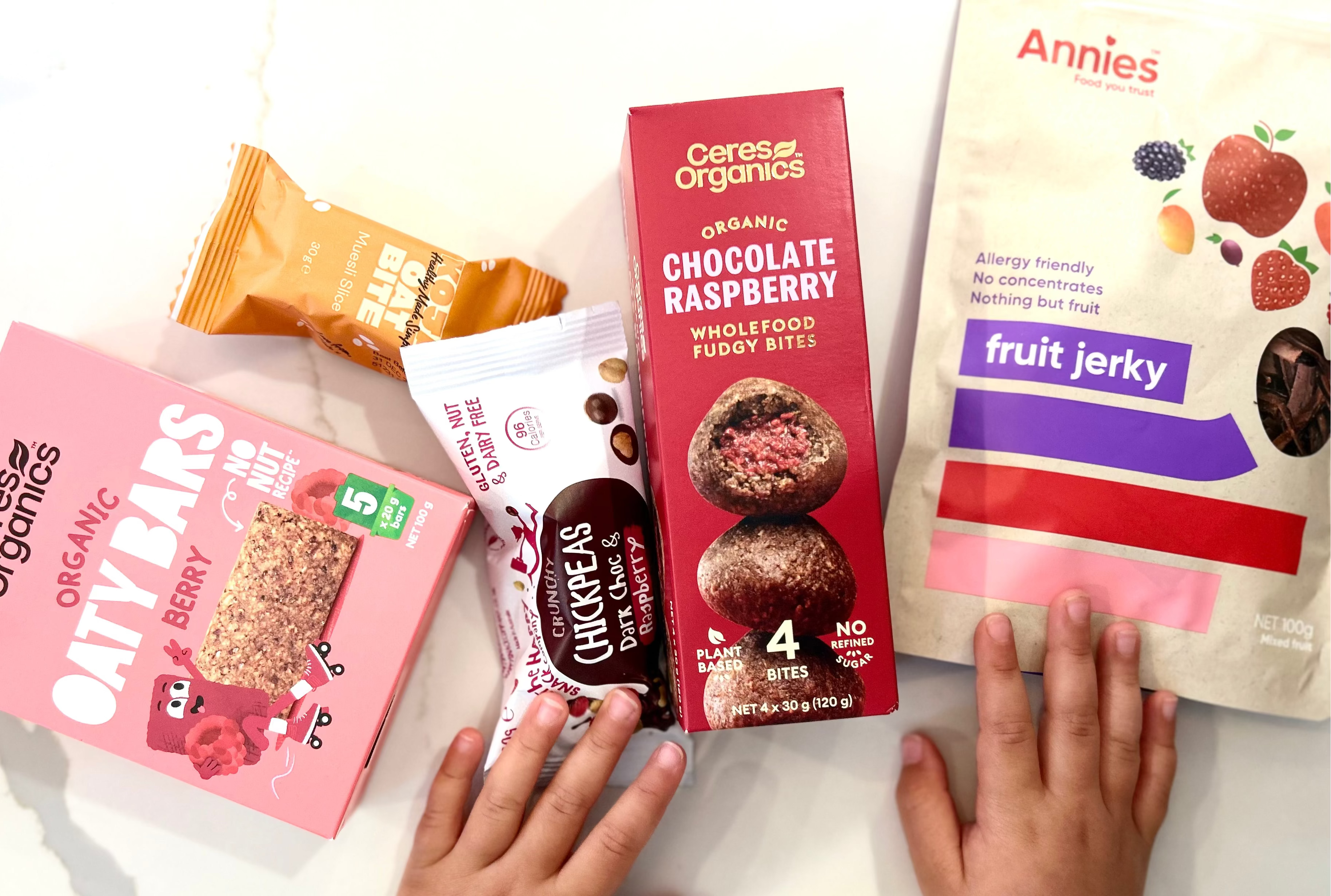 Assorted snack packages including Ceres Organics and Annie's with child's hands reaching towards them.

