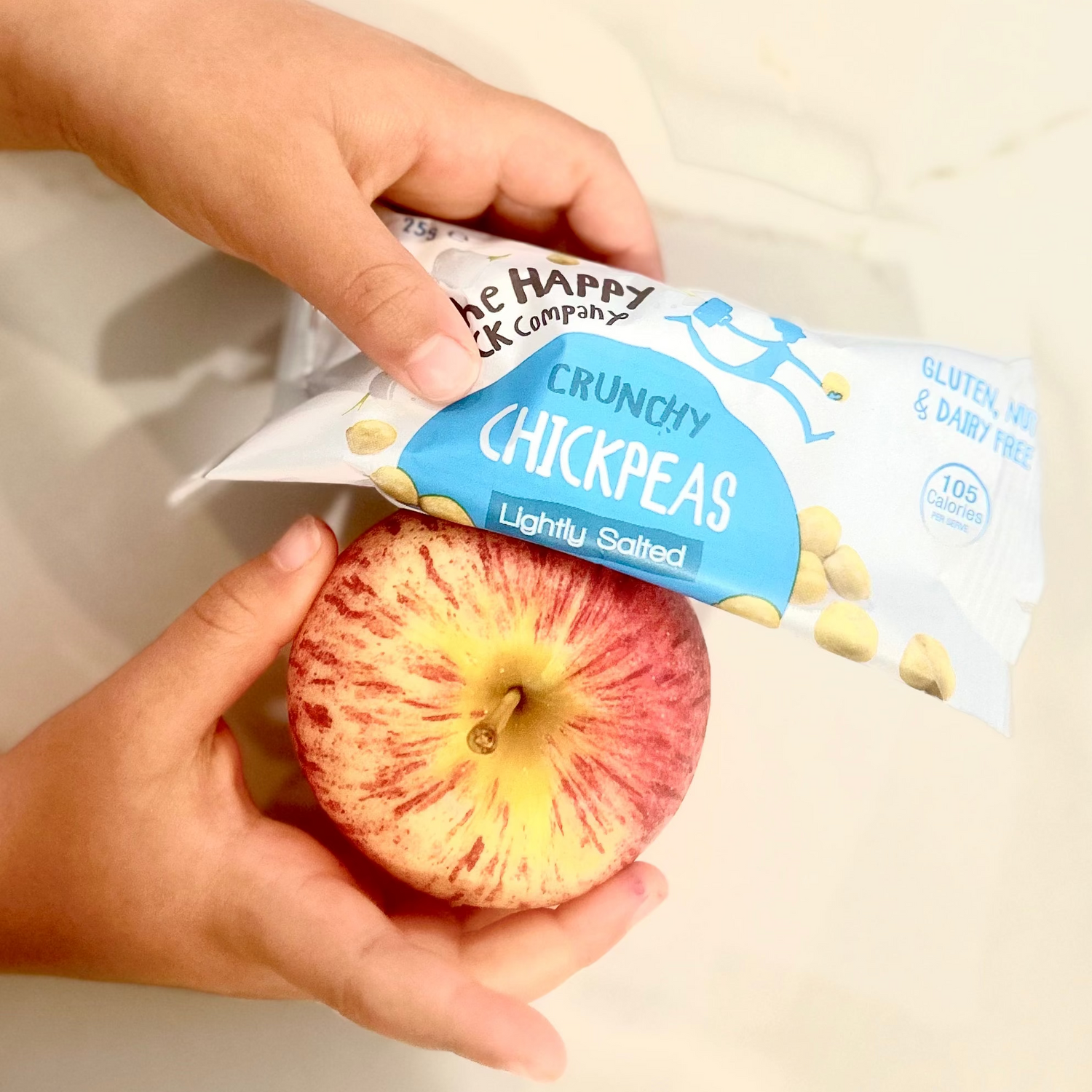Hand holding a bag of crunchy chickpeas and an apple from a school lunchbox